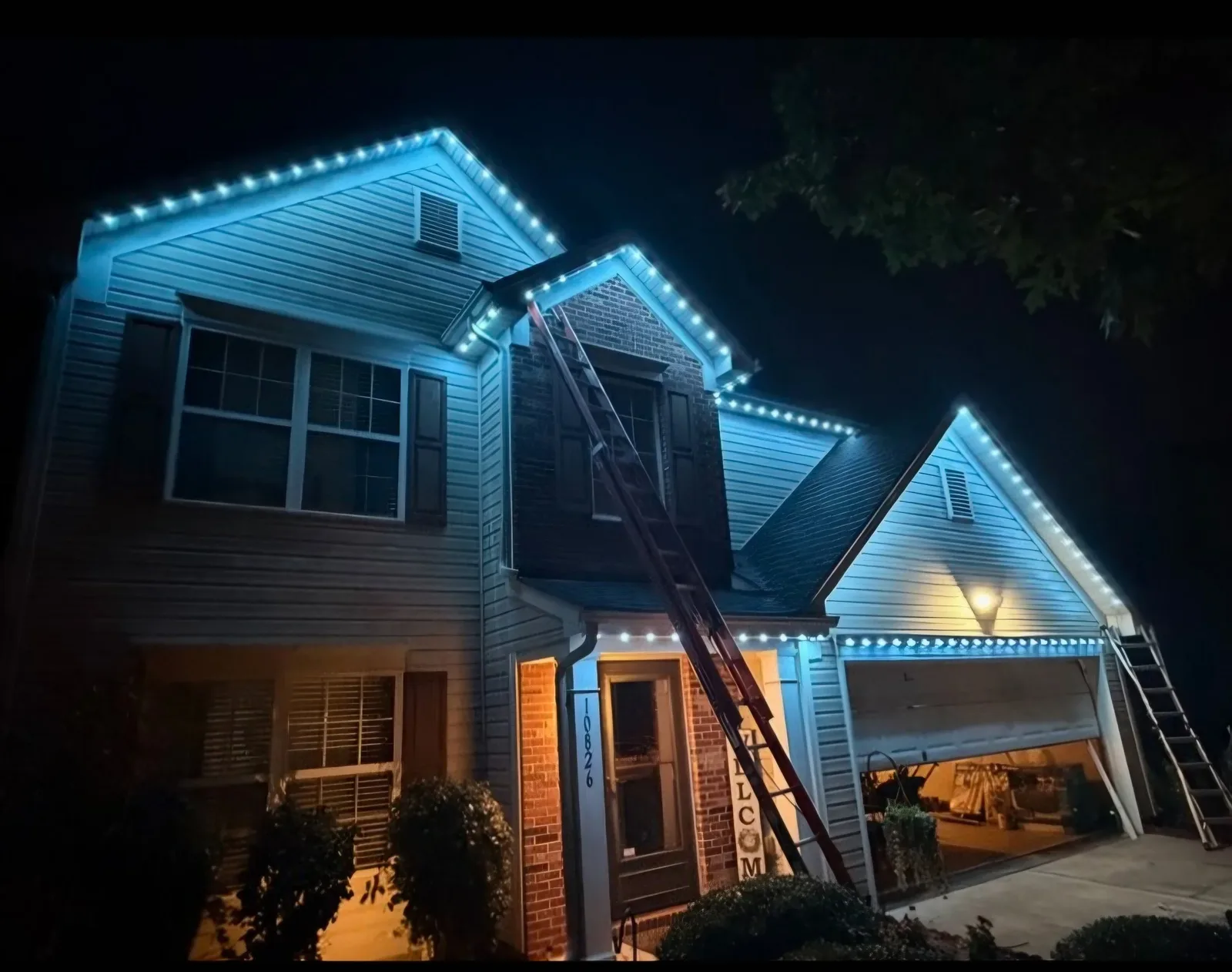 Two-story home lit in blue with the install crew's ladders still up