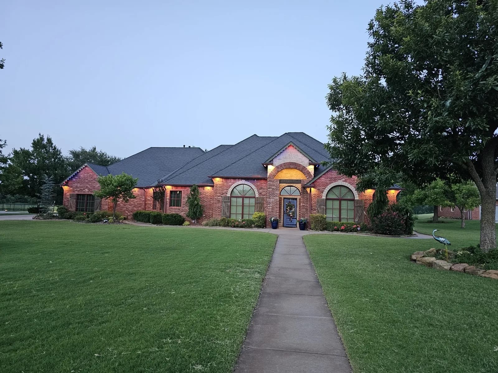 Brick home in warm white permanent lighting with a long front lawn at dusk